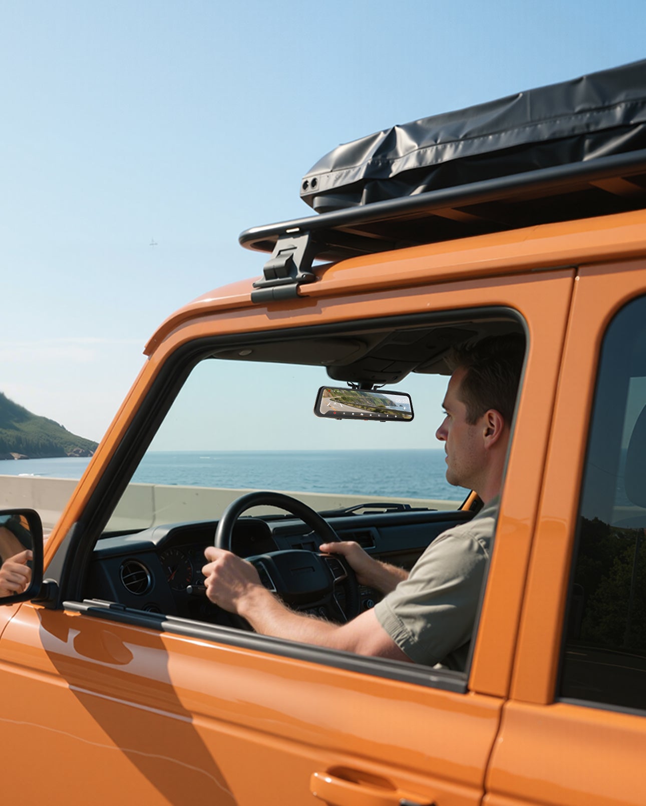 Man driving an orange vehicle with a roof rack near a coastal area